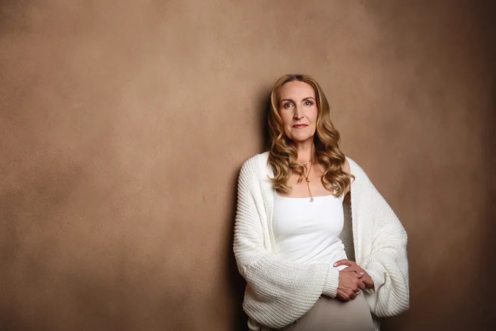 Frau ab 50 in heller Strickjacke vor braunem Hintergrund
