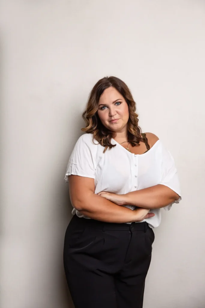 Fotografin Lisa Schmalzer lehnt an einer weißen Wand, Arme verschränkt