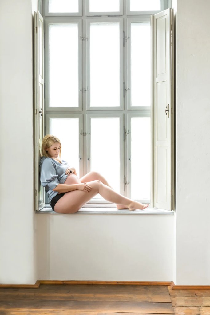 Schwangere im Blazer schaut aus dem Fenster