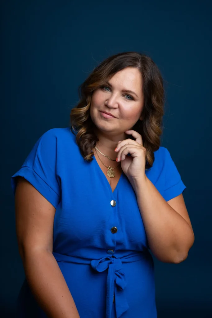 Fotografin Lisa Schmalzer schaut in die Kamera, blaues Kleid vor dunklem Hintergrund