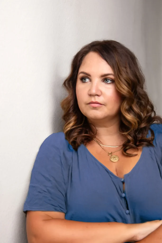 Lisa Schmalzer lehnt an einer weißen Wand und schaut zur Seite