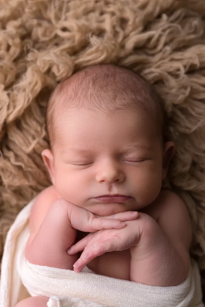 Baby in Creme, Hände am Kinn